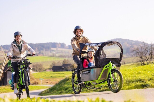 A family rides with cargo bikes from Radkutsche through hilly terrain, with accessories from Vaude