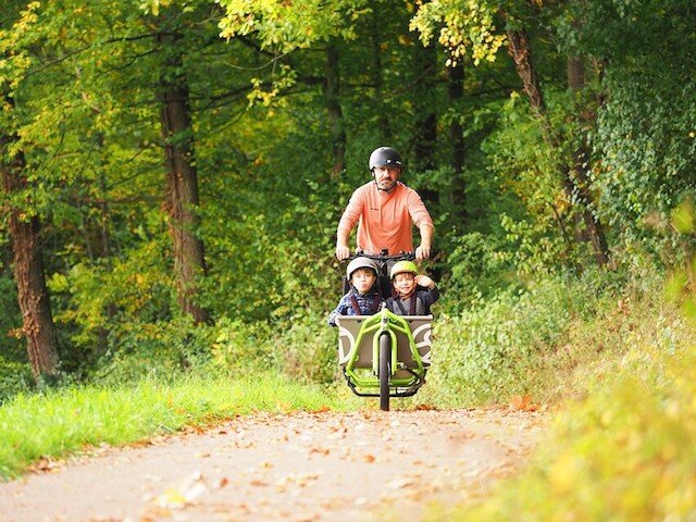 Father with 2 childeren drives on there e cargo bike thourgh the woods