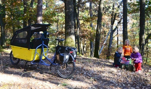 Childeren play in the woods next to a blue cargo bike with yellow box from Radkutsche