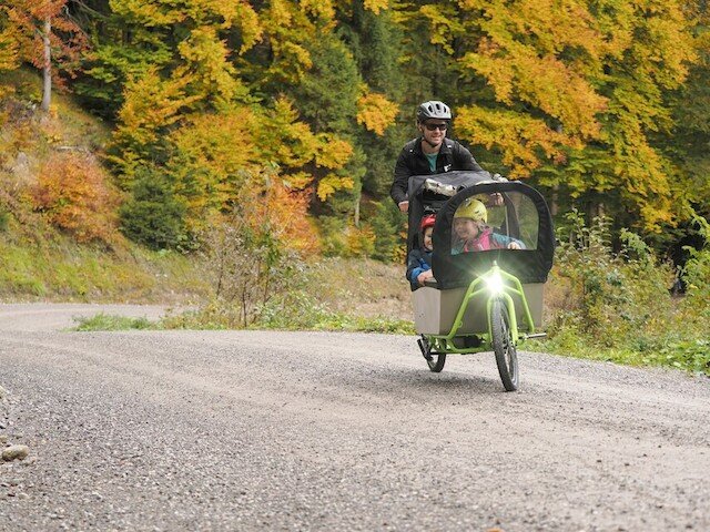 Family drives with their cargo bike over gravel road on steep hill in the forest