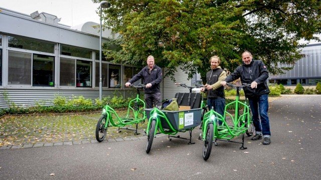 Three men with green Radkutsche cargo bikes outside a modern building