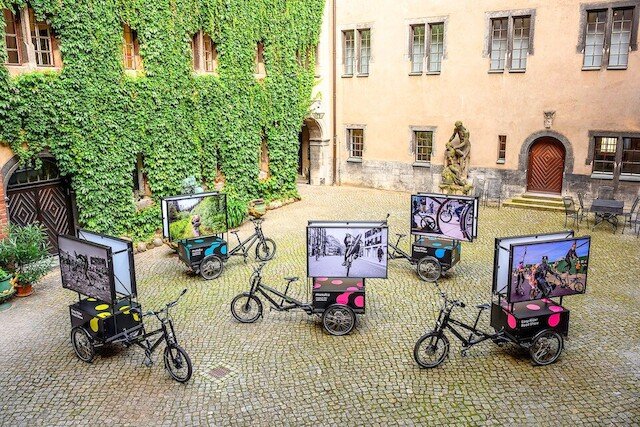 5 three wheeled cargo bikes from Radkutsche stand on a square with old buildings on the background