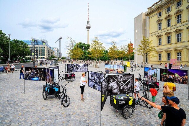Five three-wheeled cargo bikes from Radkutsche GmbH are parked in a market square in Berlin.