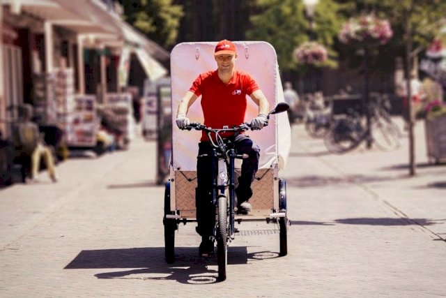 A garbage man drives on his three-wheeled cargo bike, which he uses to collect rubbish from shops