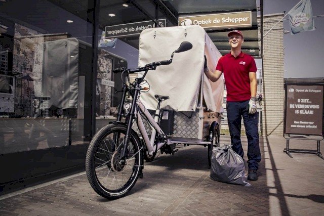 A garbage man stands next to his three-wheeled bicycle, which he uses to collect rubbish from shops