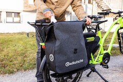A grey Vaude bike bag with reflectors and logo print hangs on a green cargo bike from Radkutsche GmbH.