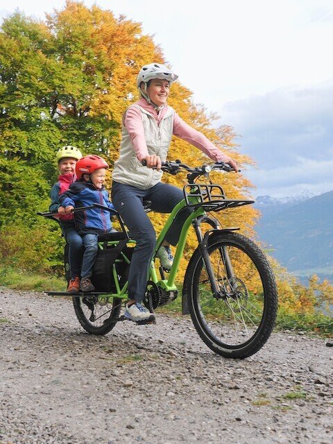 Mother with two childeren driving a long tail cargo bike from Radkutsche over a gravel road in the mountains