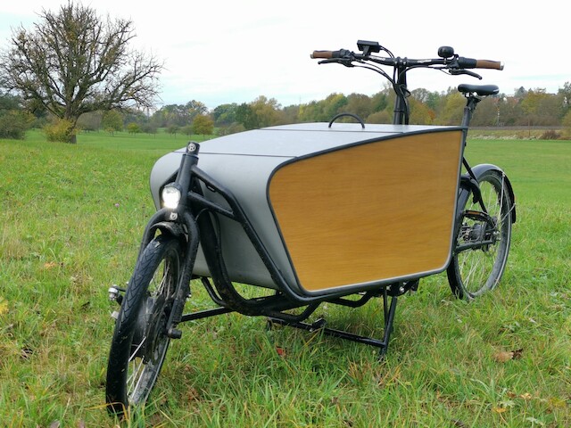 Ein schwarzes Lastenrad Rapid von Radkutsche steht auf einer grünen Wiese mit einem Holzaufbau, den ein Kunde selbst gebaut hat.