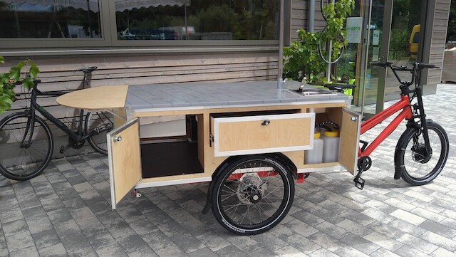 Ein roter Musketier von der Manufaktur Radkutsche wird mit einer Koch- und Gastronomieausstattung gezeigt, mit vielen Schubladen und Klapptischen für maximale Effizienz und Platz.
